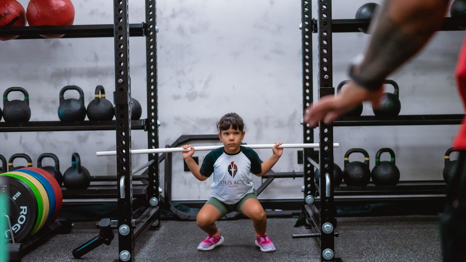 A child squatting with a training bar while a coach spots