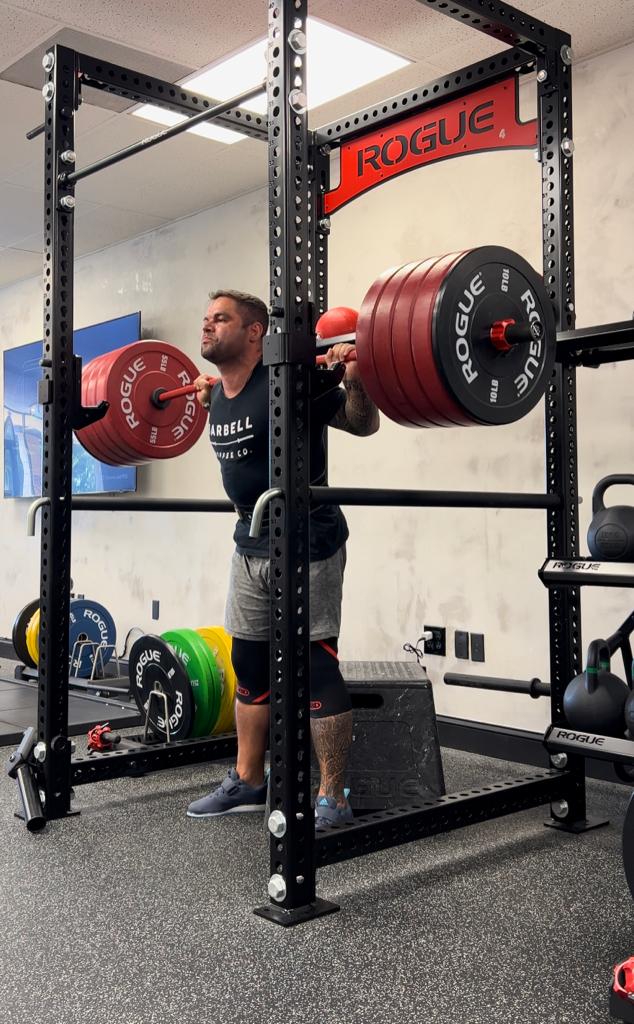 A member squatting under a loaded barbell in the rack